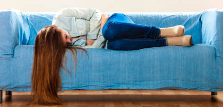 Loneliness negative emotion concept. Young sad stressed woman lying on couch at homeの写真素材