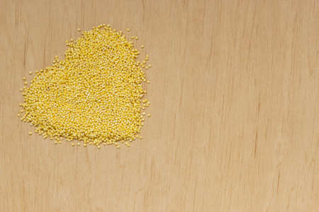 Dieting healthcare concept. Millet groats heart shaped on wooden surface. Healthy food gluten-free and highly alkaline.の写真素材