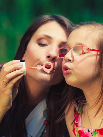 Mother and little girl daughter child blowing soap bubbles outdoor. Parent and kid having fun in park. Happy and carefree childhood. Good family relations.の写真素材