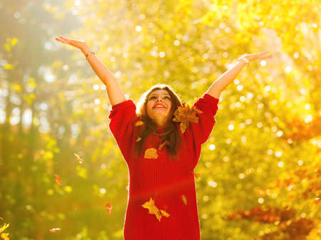 Happiness carefree. woman relaxing in autumn park throwing leaves up in the air with arms raised up. Beautiful girl in colorful forest foliage outdoor.の写真素材