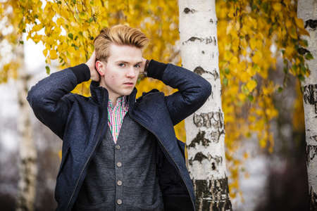 Fall season and people concept. Portrait of young stylish fashionable man in plaid shirt and jacket against autumn birch trees. Yellow leaves backgroundの写真素材