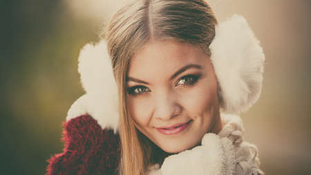 Portrait of pretty smiling fashionable woman in fall forest park. Happy gorgeous young girl in white earmuffs and sweater pullover. Autumn winter fashion.の写真素材