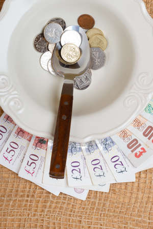 Cost of living, price of food and eating wealth concept. British money on kitchen table, plate spoon with coins and banknoteの写真素材