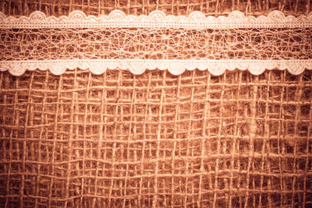 White lace ribbon on brown mesh material, natural burlap backgroundの写真素材