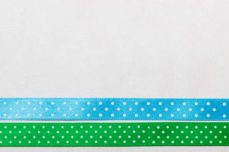 Festive celebration party frame. Polka dot green blue satin ribbon on white cloth backgroundの写真素材