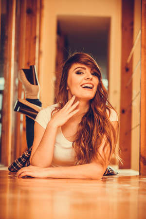 Happy cute pretty gorgeous woman laying on floor at home. Attractive young girl with long hair wearing white shirt and jeans. の写真素材
