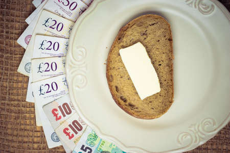 Cost of living, food budget concept. British money on kitchen table, plate with piece of bread...