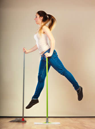Cleanup housework concept. Funny cleaning lady young woman mopping floor, holding two mops new and old jumpingの写真素材