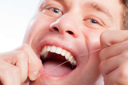 Daily health care. Young man cleaning flossing his white teeth with dental floss