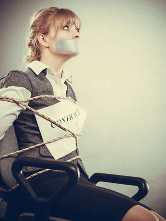 Afraid businesswoman bound by contract terms and conditions with mouth taped shut. Scared woman tied to chair become slave. Business and law concept. filtered.の写真素材