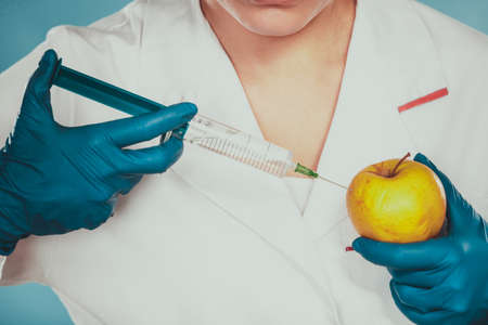 Scientist doctor injecting apple with syringe. Chemist holding genetically modified fruit. GM food modification.の写真素材