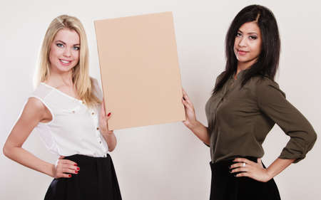Advertisement concept. Two women caucasian and african holding blank board empty banner cardboard studio shotの写真素材