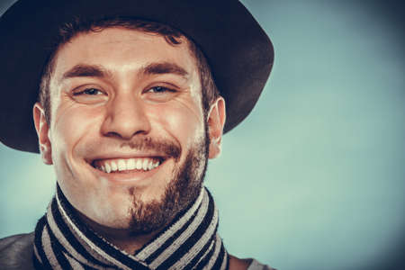 Portrait of happy man with half shaved face beard hair in hat and scarf. Smiling handsome guy on blue. Skin care hygiene and fashion. の写真素材