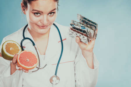 Dietitian nutritionist woman holding diet weight loss tablets pills and grapefruits. Choice between natural and synthetic way of slimming dieting. Health care.の写真素材