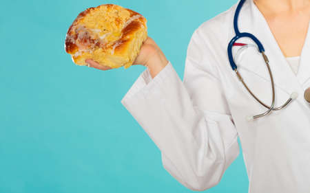 Dietitian nutritionist holding sweet roll bun. Woman with fattening junk food. Bad unhealthy eating nutrition concept.の写真素材