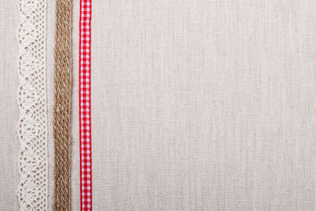 Lace, rope and red ribbon frame on natural linen, bright cloth fabric background. Retro styleの写真素材