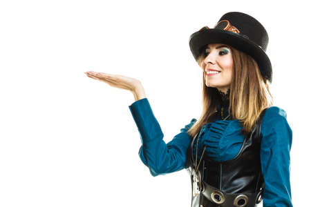 Smiling young steampunk islolated girl on white holding fancy rifle with open hand plam. Fantasy old fashion wearing hat and goggle.の写真素材