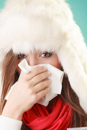 Sick woman in fur hat sneezing in tissue. Ill girl caught winter cold flu in studio on green.の写真素材