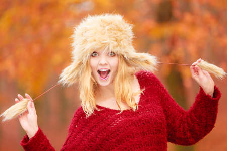 Portrait of pretty smiling fashionable woman in fall forest park. Happy gorgeous young girl in fur winter hat and sweater pullover. Autumn fashion.の写真素材