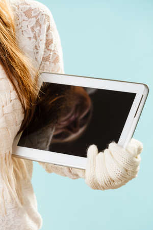Young woman holding xmas gift. Girls hands in woolen white gloves showing screen of tablet. Christmas time concept.の写真素材