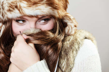 Winter female fashion. Portrait of beautiful young lady in fur cap on grey background in studio.の写真素材