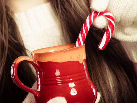 Christmas helping giving concept. Close up of woman hands holding red mug with beverage and sweet cane.の写真素材