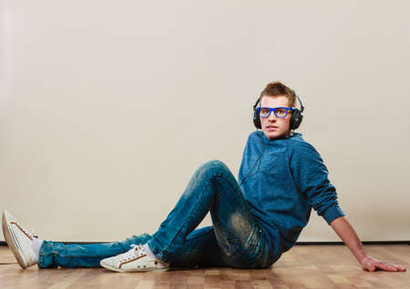 leisure and lifestyle concept. Young hipster man fashion clothes with headphones sitting on floor listening music.の写真素材