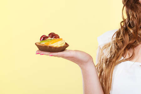 Bakery sweet food and people concept. fruit cake cupcake on woman hand yellow backgroundの写真素材