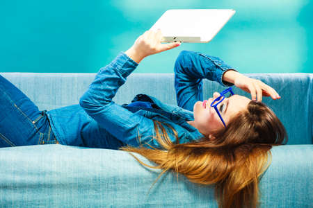 Modern technology education internet concept. Fashion student girl in glasses with tablet relaxing on blue colorの写真素材