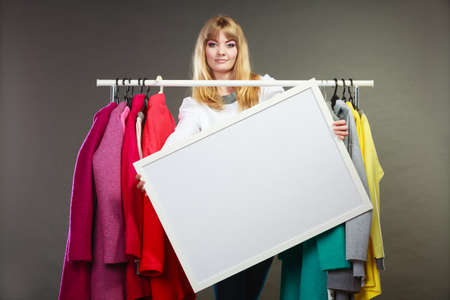 Pretty woman in wardrobe holding blank empty banner. Gorgeous girl customer in mall shop with copyspace. Fashion clothing sale advertisement concept.の写真素材