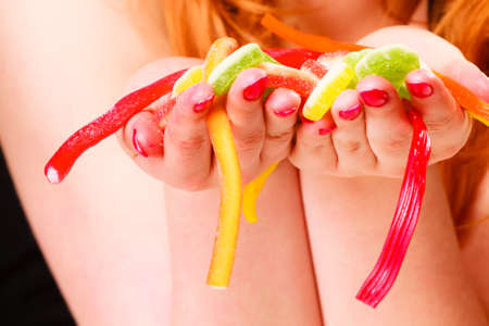 Candy addiction. Multi colored jelly sweets in red haired woman hands. Studio shot.の写真素材