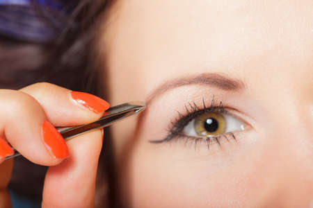 Closeup part of face, woman plucking eyebrows depilating with tweezers. Girl tweezing eyebrows.の写真素材