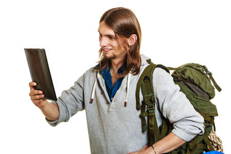 Backpacker man using pc computer tablet browsing surfing the internet. Young hiker backpacking....
