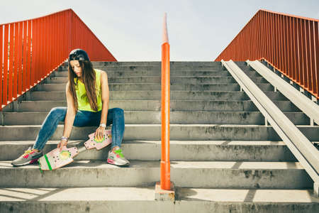 Cool young long haired girl with skateboard sitting on the urban stairs. Active lifestyle funky in summer. Trendy sport teen.の写真素材