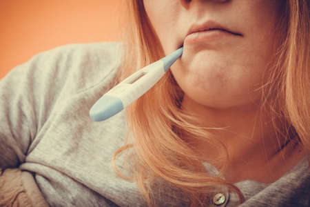 Sick ill woman with digital thermometer in mouth. Young girl having high fever measuring temperature. Health.の写真素材