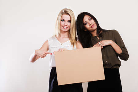 Advertisement concept. Two women caucasian and african with blank board empty banner pointing with finger studio shotの写真素材