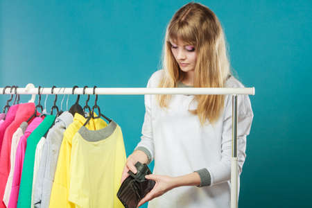 Pretty woman looking into empty wallet wants clothing from wardrobe. Young undecided shopper girl spend all money for clothes. Shopaholic concept.の写真素材