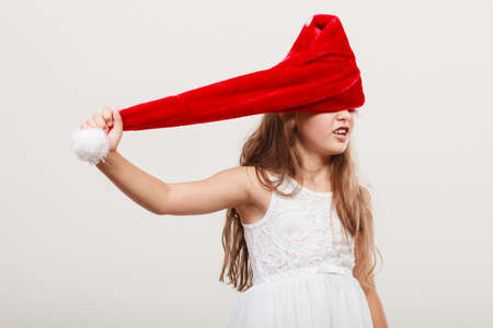 Cute little girl kid in red santa claus hat and white dress. Chrtistmas holiday season.の写真素材