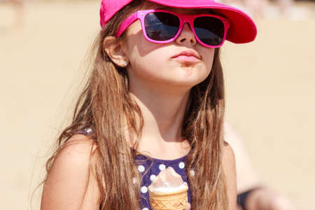 Kid eating gelato soft serve ice cream on beach. Little girl in sunglasses enjoying summer holidays vacation outdoor.の写真素材