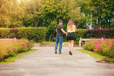 Dating. Young couple in love holding hands in summer park outdoor. Back view.の写真素材