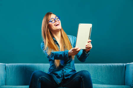 Modern technologies leisure and young people concept. fashionable woman wearing jeans with tablet sitting on couch blue colorの写真素材