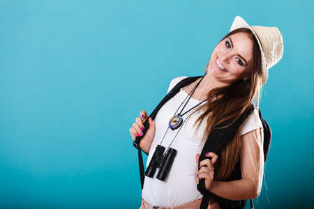 Summer vacation and tourism concept. Young woman in straw hat with backpack binocular compass on blue portraitの写真素材