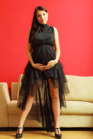 Stylish pretty girl in black evening dress. Pregnant woman preparing for event. Prospective mothering concept.の写真素材