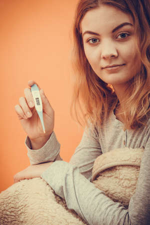 Sick ill woman under blanket with digital thermometer. Young girl having high fever measuring...