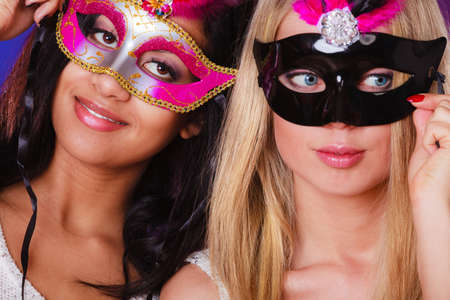 Holidays, people and celebration concept. two women mixed race and caucasian with carnival venetian masks over festive background.の写真素材