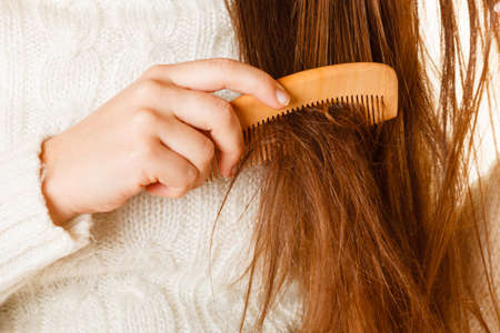 Female hand combing with brush her dry damaged long hair. Daily preparation for looking nice.の写真素材