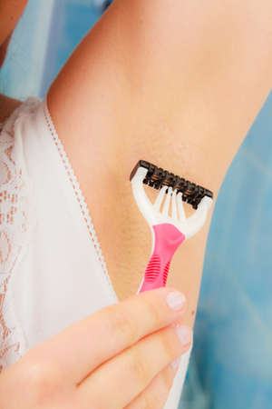 Hygiene skin care concept. Closeup woman shaving armpit with razor in bathroomの写真素材