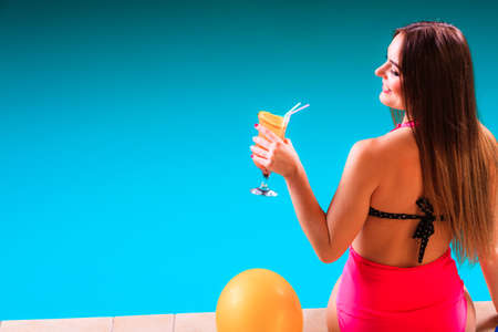 Spa relax and holidays concept. Young woman in swimsuit rear view. Fit female body, girl sitting at poolside holding cocktail glass in handの写真素材