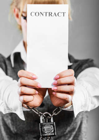 Business concept. Serious woman businesswoman with chained hands holding contract, side view grungy backgroundの写真素材