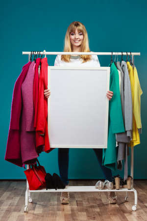 Woman in wardrobe holding blank empty banner. Girl customer in mall shop with copyspace. Fashion clothing sale advertisement.の写真素材